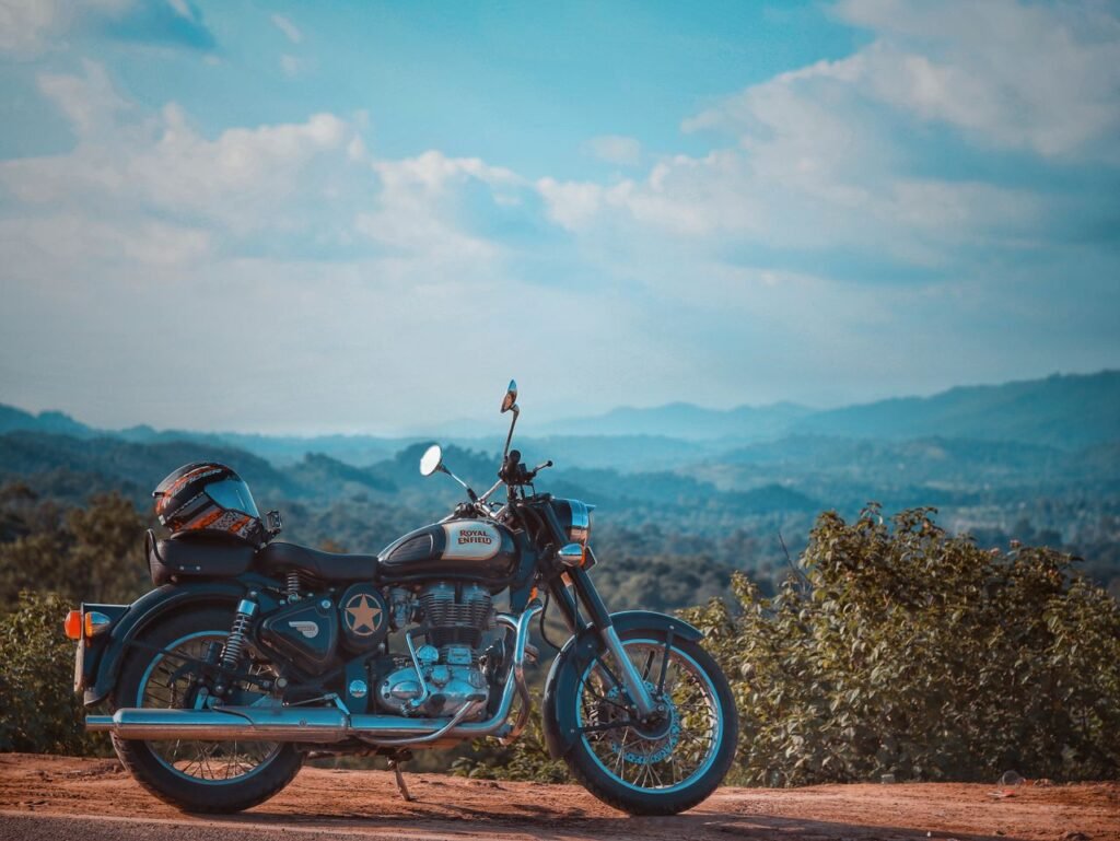 A classic Royal Enfield motorcycle parked against a scenic mountain backdrop under a clear blue sky.